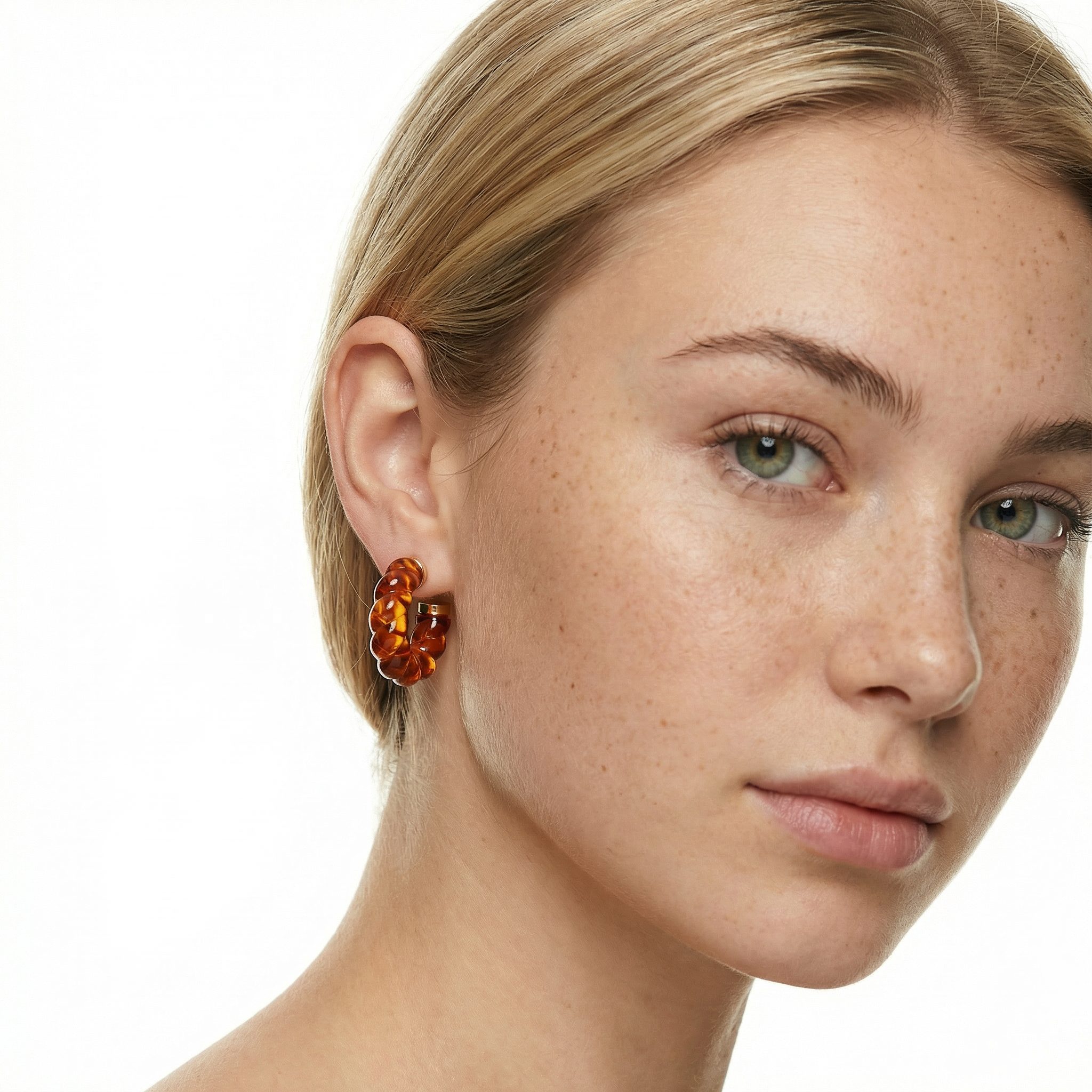 Transparent twisted geometry hoop earrings in red orange burnt amber with gold-toned electroplated stainless steel studs worn on model