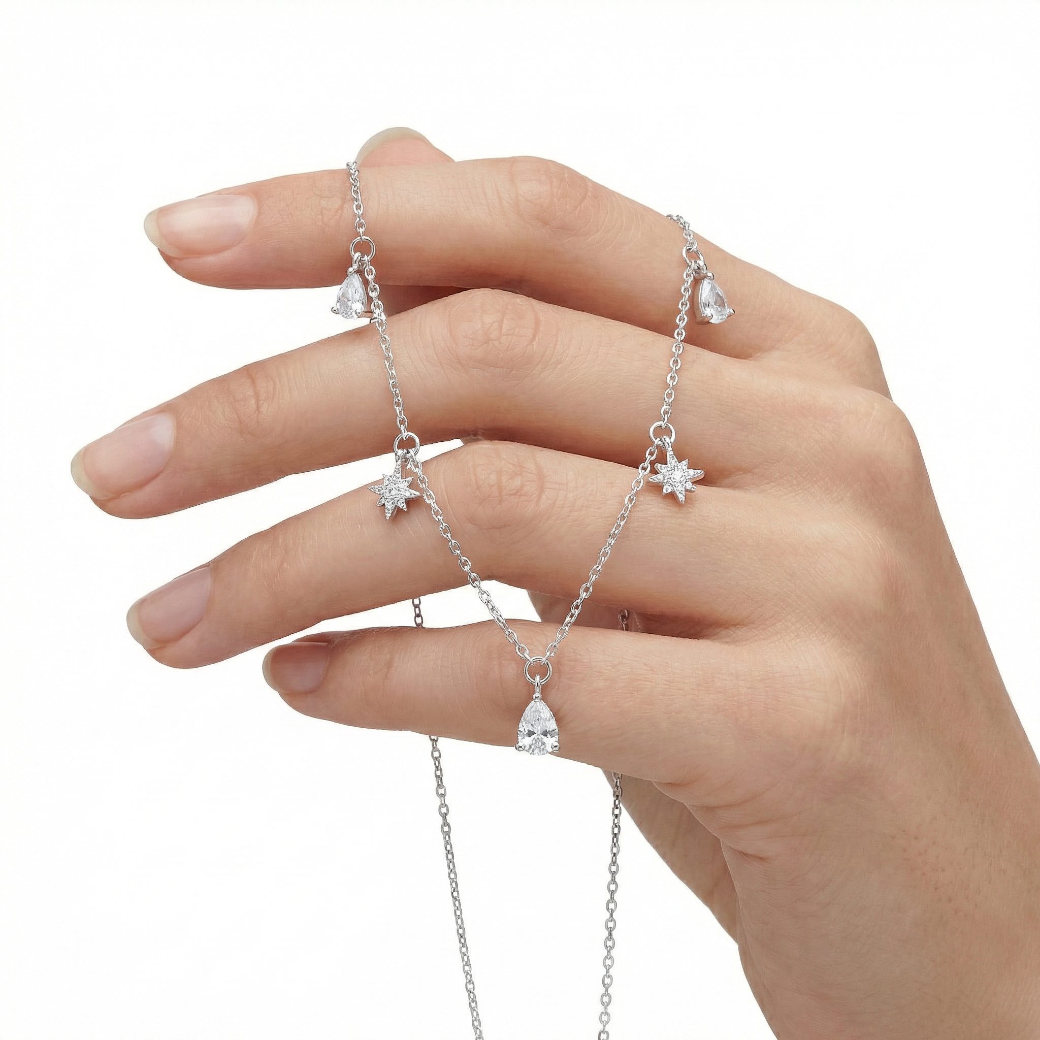 Hand holding a delicate sterling silver zircon necklace with star and water-droplet charms, lightweight women’s jewellery